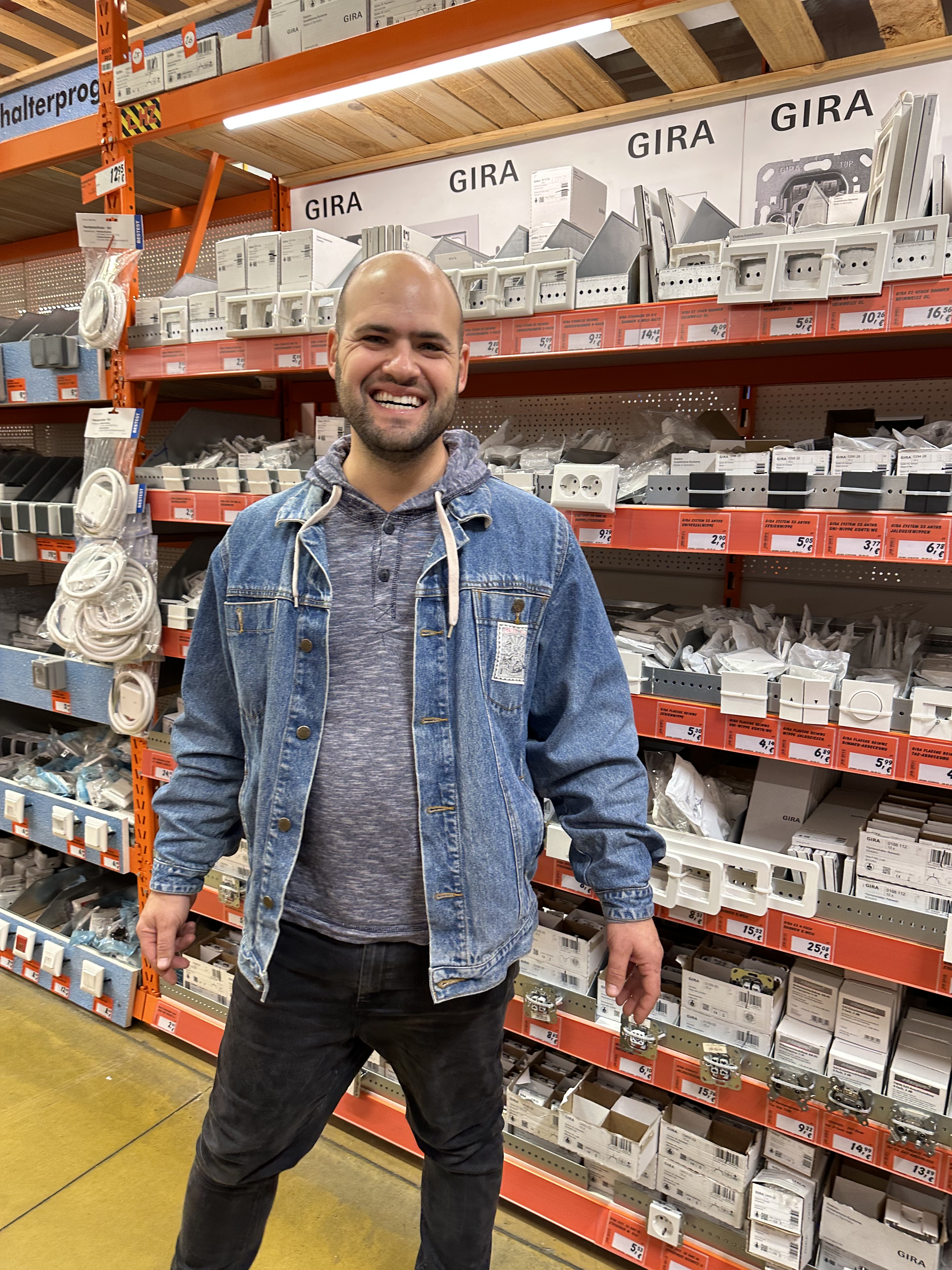 Avi smiling in front of electrical products in a Berlin hardware store