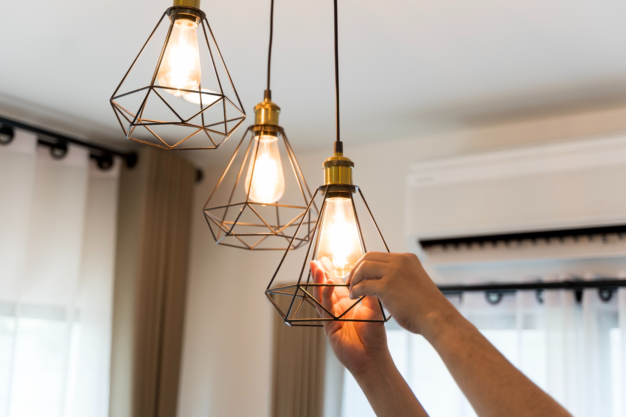 Hands adjusting a set of modern geometric pendant lights in a Berlin home.