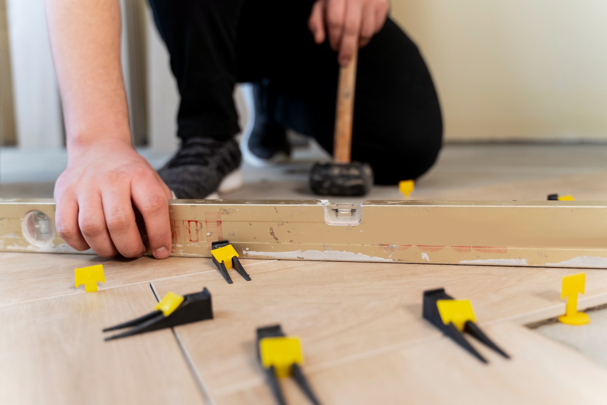 Floor installer checking tile alignment with a long spirit level and spacers.