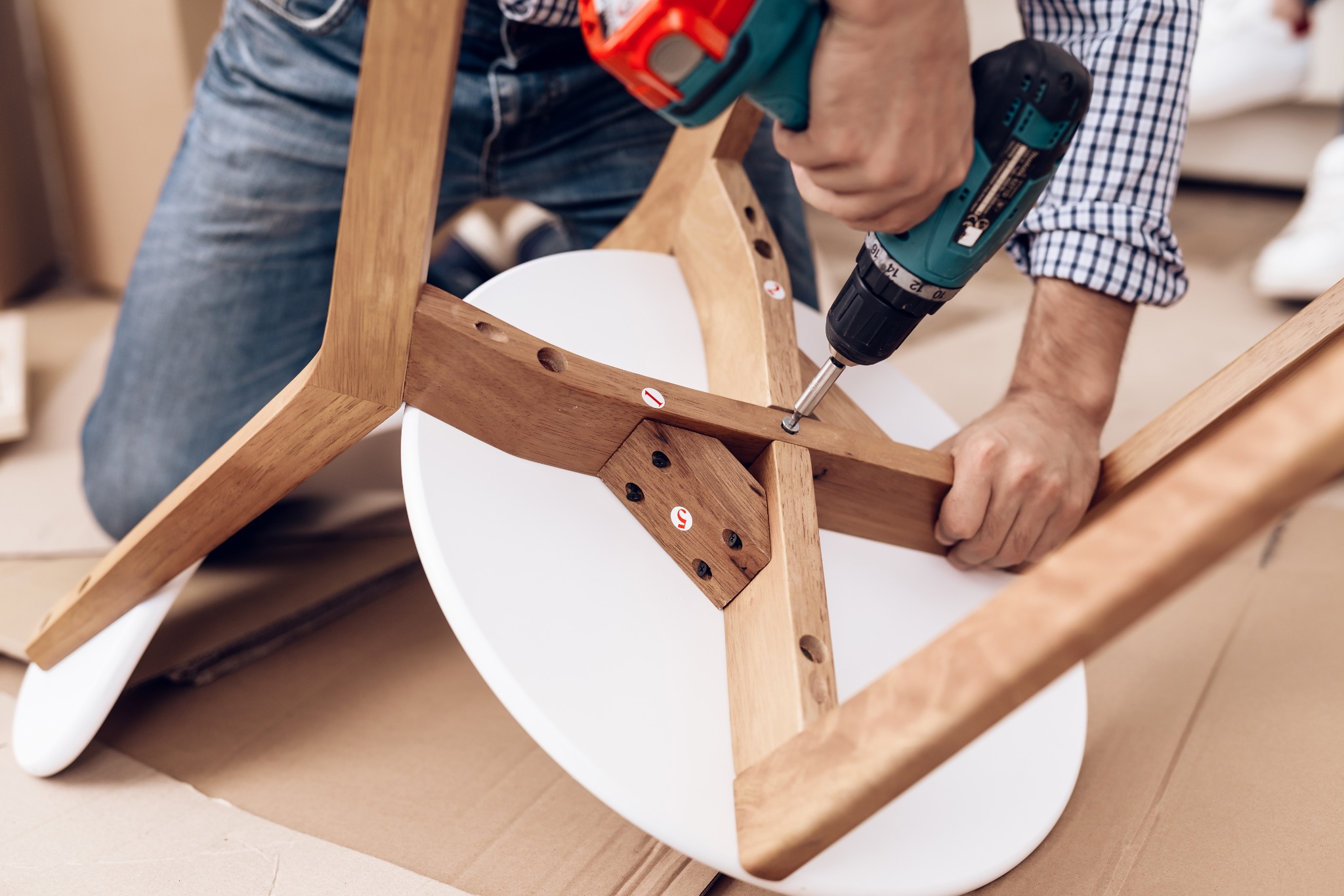 Furniture assembler securing the wooden frame of a chair with a cordless drill.