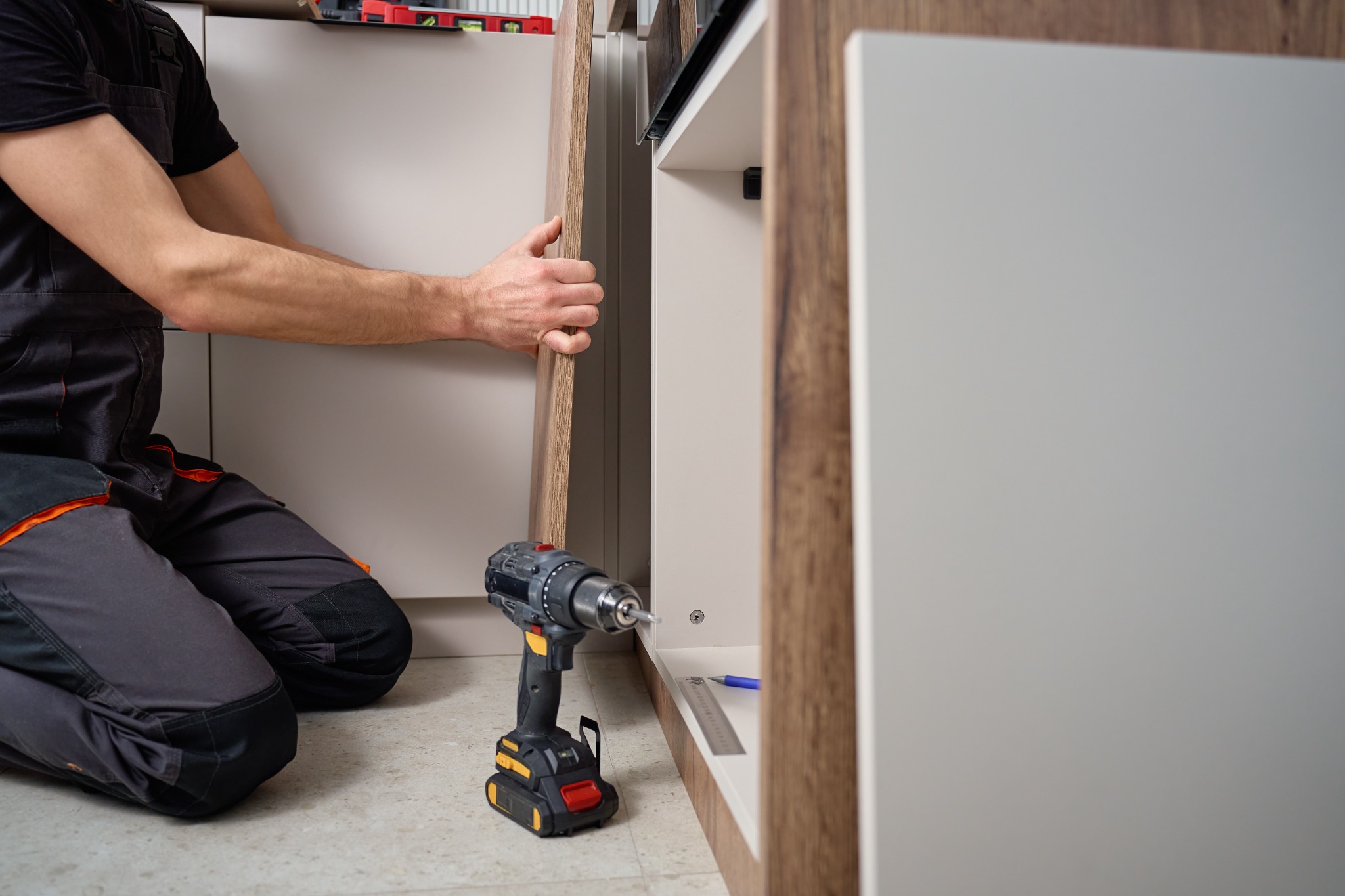 Kitchen installer fitting a wooden cabinet door beside built-in appliances.