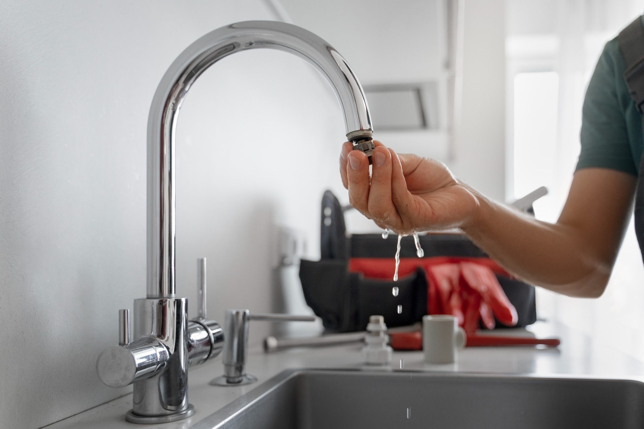Plumber repairing a dripping chrome kitchen tap beside a sink.