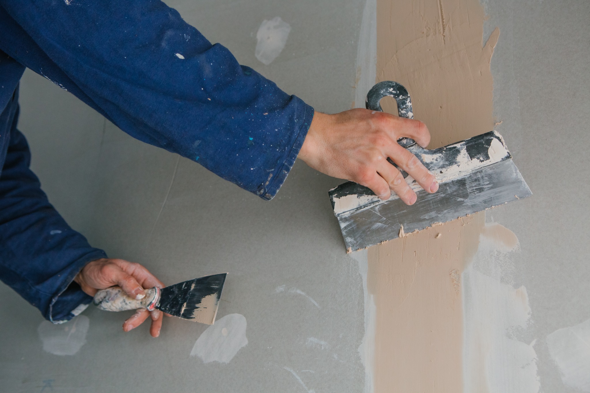 Handyman applying smooth plaster to a wall with two finishing trowels.